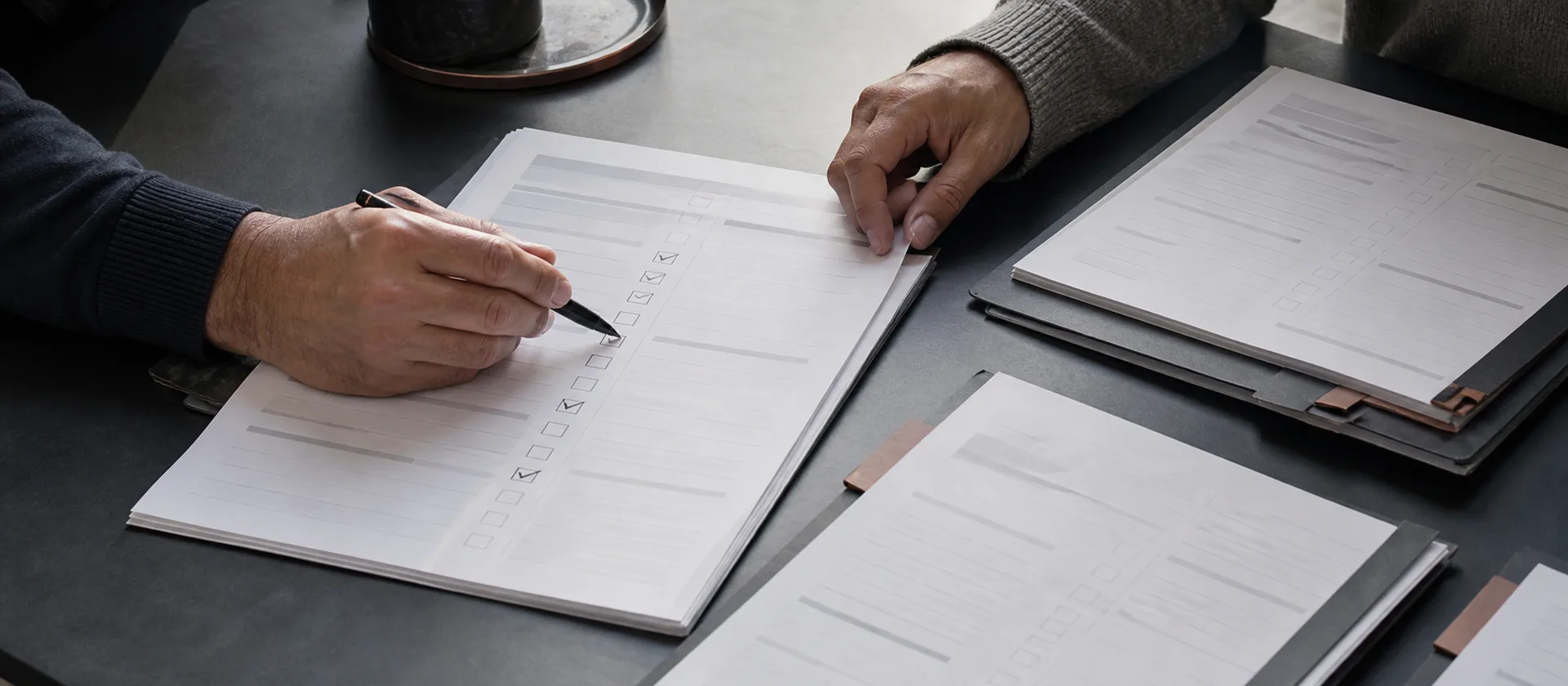 Two people mark a month-end close checklist beside a set of generic statement packets.